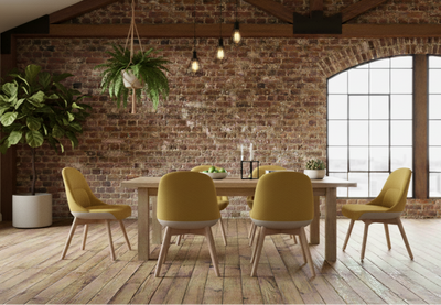 Bloom Scandi Four Leg Chairs by Quell Design in vibrant yellow upholstery arranged around a natural oak dining table in a bright contemporary room with exposed brick walls, oak floors, large windows, and lush green plants. Featuring smooth contoured seats upholstered in linen velvet with eco-friendly leather detailing and natural beech wood legs, these Scandinavian-inspired chairs bring warmth, comfort, and modern elegance to the dining space.