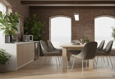 Bloom Chairs by Quell Design in soft light grey upholstery arranged around a wooden table in a contemporary hospitality setting with exposed brick walls, large industrial-style windows, and warm wooden floors. These modern ergonomic chairs feature a sculpted seat with linen-velvet and eco PU panels on slim black steel legs, blending comfort, texture, and minimalist elegance for restaurants, lounges, or hotel spaces.