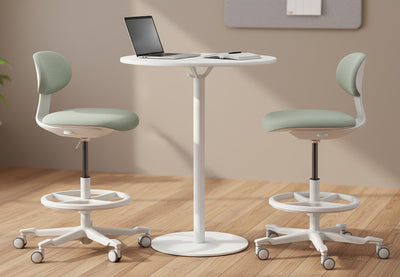Toro Pivot Motion Office Stools shown in a contemporary interior setting, with two stools positioned around a tall round table on a wooden flooring, complemented by beige walls and greenery, highlighting modern ergonomic office stools designed for collaborative and flexible workspaces.