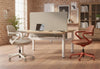 Kubo Contemporary Desk Chairs in coral red and beige displayed together in a modern office interior, featuring tall windows, high ceilings, exposed brick walls and wooden flooring, highlighting ergonomic seating design and contemporary workplace aesthetics.