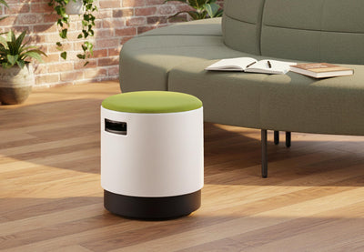 Ikon Rounded Comfort Stool featured in a contemporary office lounge, positioned in front of a Hage circular sofa, with wooden flooring, exposed brick walls and greenery, showcasing modern breakout seating for collaborative and relaxed work environments.