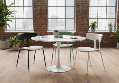Three Okse Nord Stackable Chairs in morandi green, white and black arranged around a collaboration table in a workspace with exposed brick walls, wooden flooring, tall windows and indoor greenery.